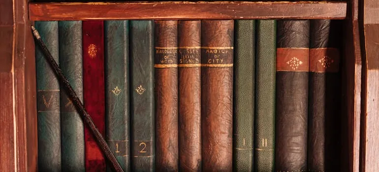 pexels-mikhail-nilov-8391470.jpg Old books on a shelf with a wand leaning against them