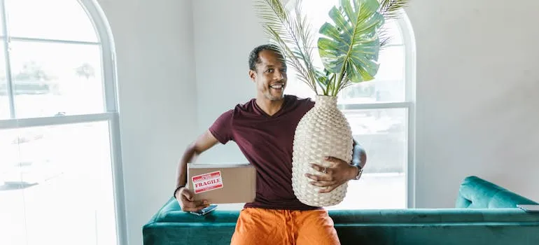 pexels-rdne-7464469.jpg Man holding a box and giant ceramic pineapple indoors near a window